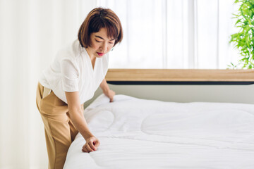 Young asian woman housewife clean bed and set up changing bedsheet with white clean sheet tidy up bedroom.room service and cleaning concept