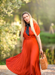 Young beautiful woman in a bright red dress walks through a blooming garden. In her hands she holds...