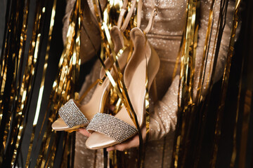 Cropped image of woman holding shoes high heels, prepare for prom ballroom party celebration.Gold...