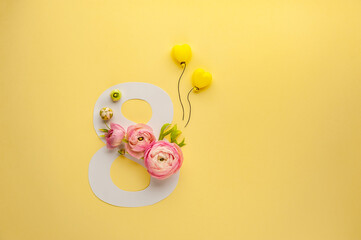 Greeting Card International Women's Day on March 8th. Pink ranunculus decorates the number eight and yellow balloons on paper background. Soft focus. Top view. Copy Space.