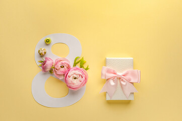 Greeting Card International Women's Day on March 8th. Pink ranunculus decorates the number eight and gift box with bow on yellow background. Soft focus. Top view.