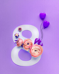 Greeting Card International Women's Day on March 8th. Pink ranunculus decorates the number eight and blank postcard on purple background. Soft focus. Top view.
