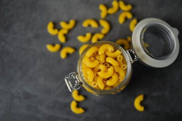 raw macaroni pasta in glass jar on black background 