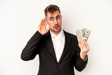 Young caucasian business man holding bank notes isolated on white background trying to listening a gossip.