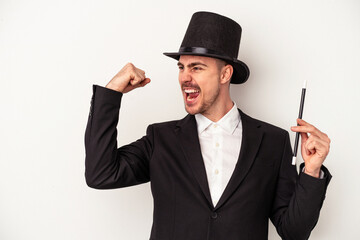 Young caucasian wizard man holding a wand isolated on white background raising fist after a...