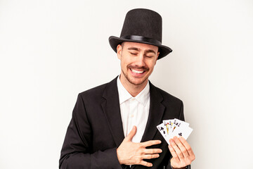 Young caucasian wizard man holding a magic cards isolated on white background laughing and having...