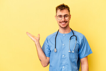 Young nurse caucasian man isolated on yellow background showing a copy space on a palm and holding...