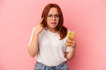 Young caucasian woman holding a mobile phone isolated on pink background showing a disappointment...