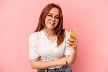 Young caucasian woman holding a mobile phone isolated on pink background laughing and having fun.