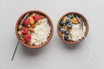 Two different Cottage cheese bowl with blueberries and raspberries, granola, almonds, walnuts and honey. Servings of healthy breakfast on light gray background