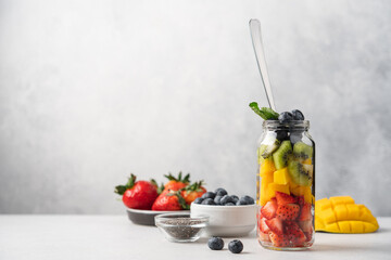 Rainbow salad of fresh fruits and berries in tall glass jar. Strawberry, mango, kiwi, blueberry pieces