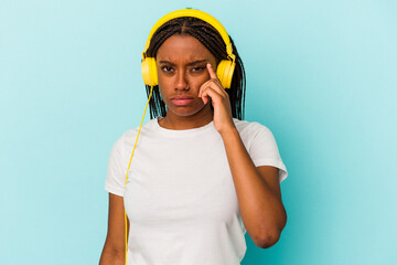 Young African American woman listening to music isolated on blue background  pointing temple with finger, thinking, focused on a task.