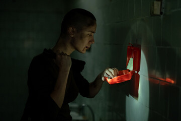 Side view portrait of tough young woman checking first aid kit and holding flashlight in dark...