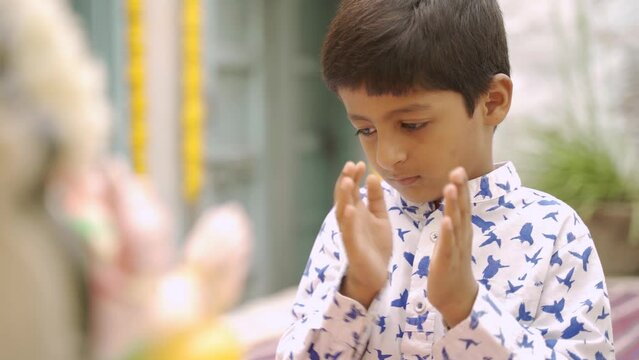 teenger playful indian kid praying to god by claping in front of god during lord ganesh festival - concept of faith in god, treditional and religious rituals.