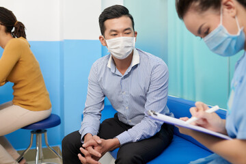 Patient in protective mask talking to medical nurse and explaining his complains and disease...
