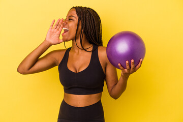 Young african american woman holding a pilates ball isolated on yellow background  shouting and...
