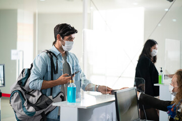 Caucasian male traveler wearing face mask giving passport to airline customer check in officer at airline service counter in airport. traveler wearing mask prevent covid-19 or coronavirus pandemic.