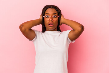 Young african american woman isolated on pink background  covering ears with hands trying not to hear too loud sound.