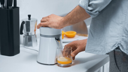 partial view of man preparing fresh orange juice in kitchen