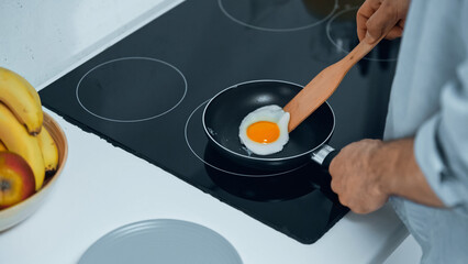 partial view of man frying egg while preparing breakfast