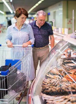 Mature family of retirees examines dried fish in the department of a supermarket