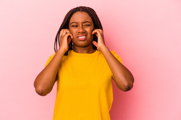 Young african american woman isolated on pink background  covering ears with fingers, stressed and desperate by a loudly ambient.