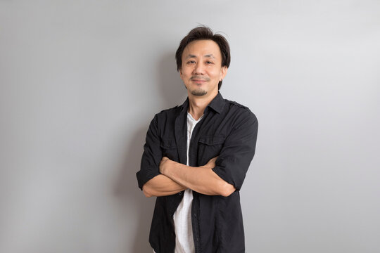 Middle age Asian man in black shirt smile on grey background.