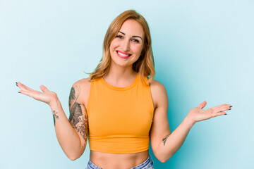 Fototapeta na wymiar Young caucasian woman isolated on blue background makes scale with arms, feels happy and confident.