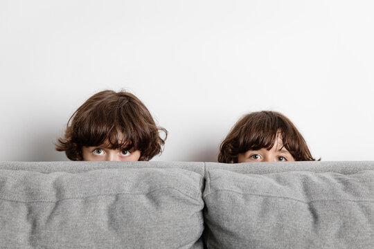 Portrait of twin brothers peeking behind couch