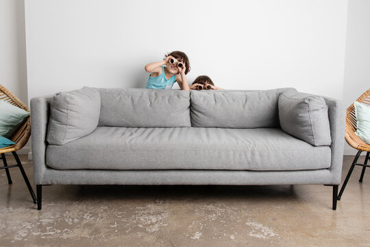 Happy Twin Brothers Hiding Behind Couch Looking Through Paper Binoculars