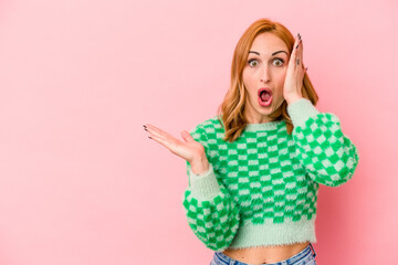 Young caucasian woman isolated on pink background impressed holding copy space on palm.