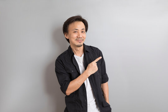 Middle Age Asian Man In Black Shirt Raising And Pointing Finger On Grey Background.