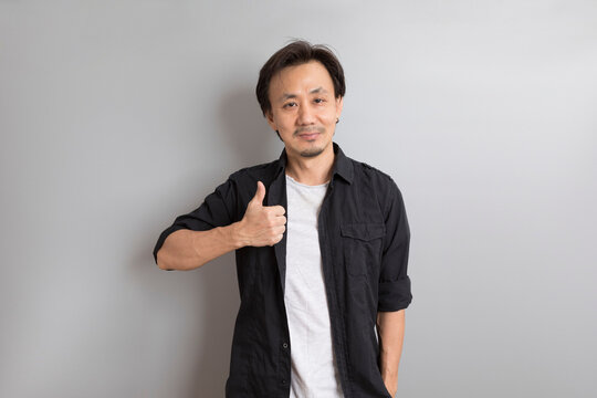 middle age Asian man in black shirt raising and pointing finger on grey background.