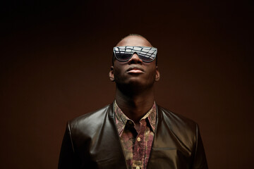 Obraz premium Portrait of African young man in stylish leather jacket and sunglasses posing on brown background