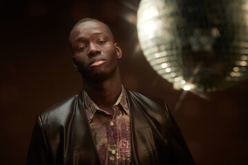 Portrait of African elegant man in leather jacket looking at camera while standing at nightclub...
