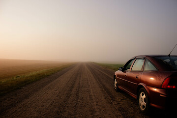 Fototapeta na wymiar Asphalt road with a parked car in the morning mist on the background of dawn.