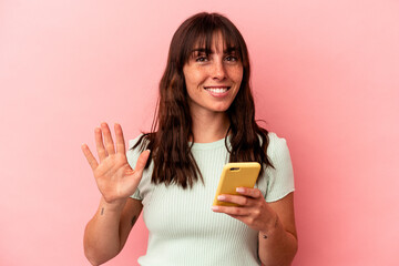 Young Argentinian woman holding a mobile phone isolated on pink background smiling cheerful showing...