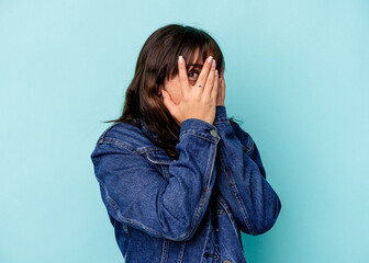 Young Argentinian woman isolated on blue background blink through fingers frightened and nervous.
