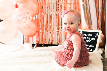 Cute birthday girl celebrating her one year birthday by messily eating a cake surrounded by pink background streamers and balloons