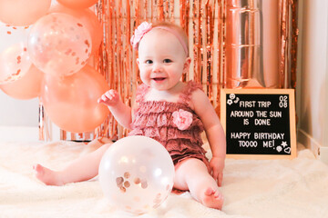 Cute birthday girl celebrating her one year birthday by messily eating a cake surrounded by pink background streamers and balloons