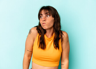 Young Argentinian woman isolated on blue background shrugs shoulders and open eyes confused.