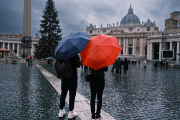 Young couple under umbrellas standing near St Peter's basilica at Vatican. Holidays for couple in...