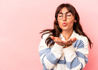 Young Argentinian woman isolated on pink background folding lips and holding palms to send air kiss.