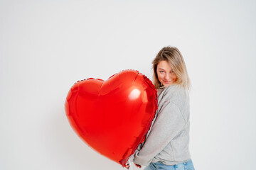 an blonde woman with a large red heart-shaped balloon on a white background. 