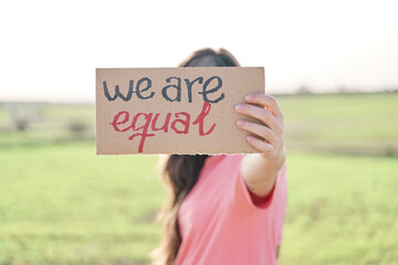 Woman holding a recycled cardboard with the inscription We are equal. Woman protesting outdoors. Concept of gender equality