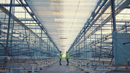 Two digital factory supervisors discussing production level in empty greenhouse