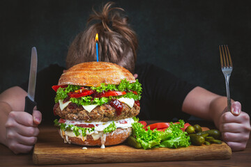 Huge burger instead of a birthday cake. Guy getting ready to eat holding a knife and fork