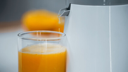 close up view of glass with orange juice near electric juicer