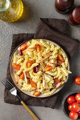 Pasta salad with grilled chicken, tomatoes and olive oil in a plate on a dark culinary background. A traditional Italian dish is girandole or fusilli with fried poultry fillet and vegetables. Top view