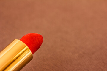 A red lipstick in golden tube on grey. Fashion background, close up, copy space, mock up